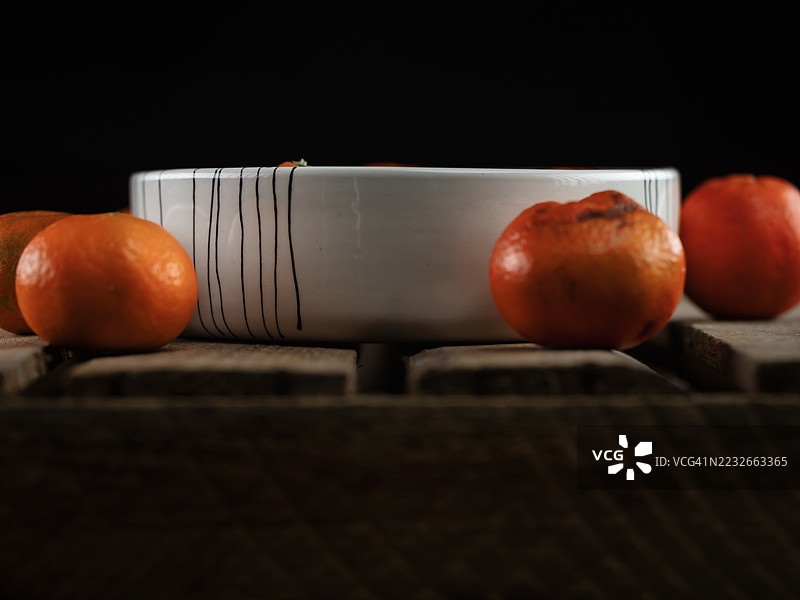 整齐剥皮的橘子放在一个陶瓷碗里，周围散落在一张古老的木桌上。图片素材