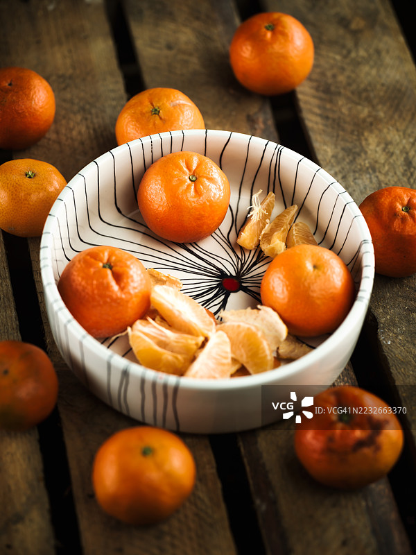 整齐剥皮的橘子放在一个陶瓷碗里，周围散落在一张古老的木桌上。图片素材