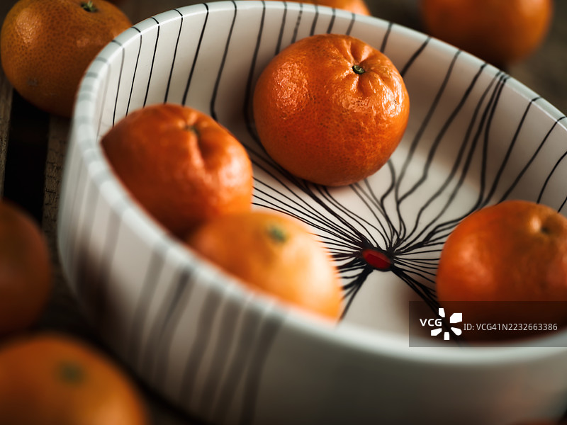 整齐剥皮的橘子放在一个陶瓷碗里，周围散落在一张古老的木桌上。图片素材