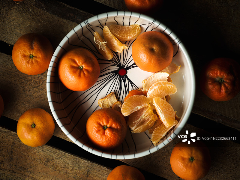 整齐剥皮的橘子放在一个陶瓷碗里，周围散落在一张古老的木桌上。图片素材