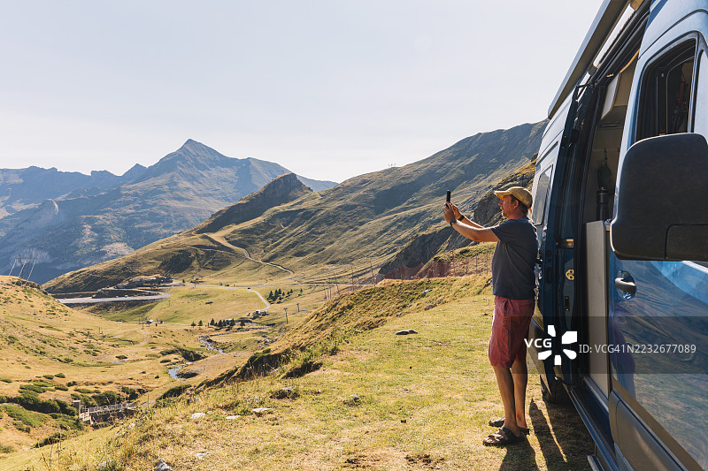 一位成熟的男士在他的房车内拍摄山景。图片素材
