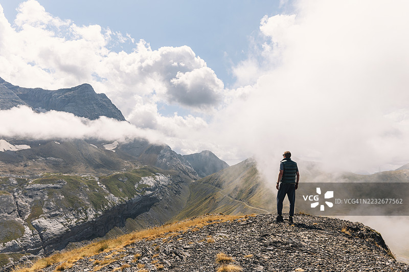 在阳光明媚的夏日，远足者背影位于法国比利牛斯山脉的高处，云层开始沿着山谷缓缓上升。图片素材