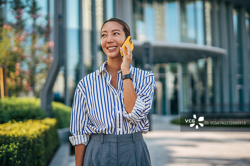 在办公大楼前微笑的女商人正在打电话图片素材
