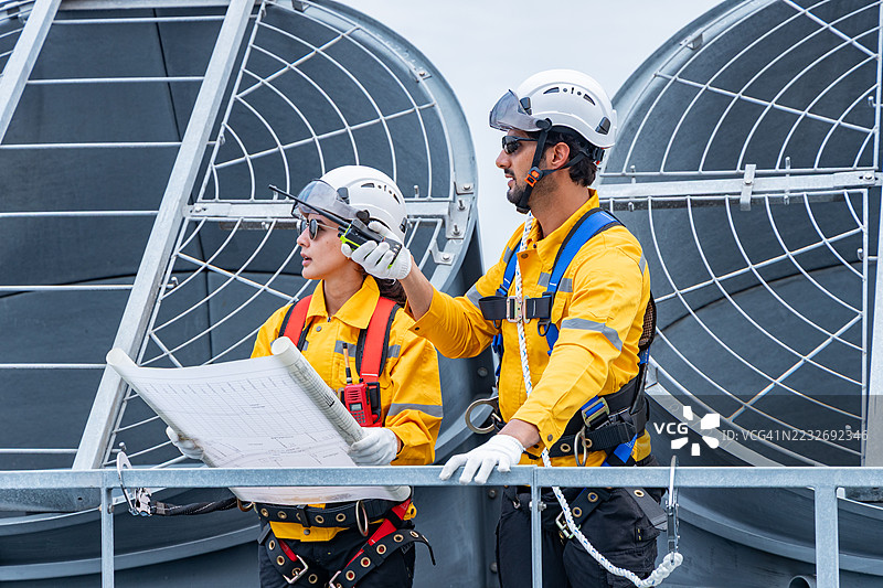 建筑师在屋顶上审查暖通空调系统的蓝图图片素材