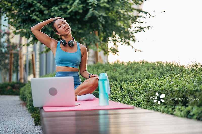 年轻女性在公园里跟随在线瑜伽课程伸展脖子图片素材