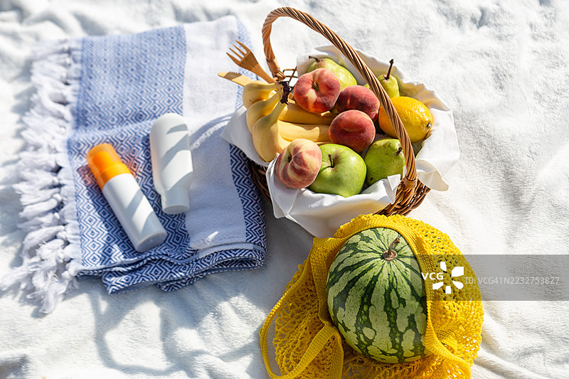 美丽的海滩野餐，篮子里的水果和旁边的防晒霜。安全的晒黑和夏季概念。图片素材