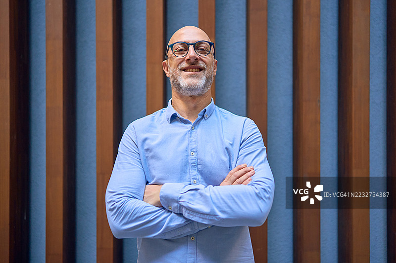 微笑的商人在现代办公室中双臂交叉摆姿势图片素材