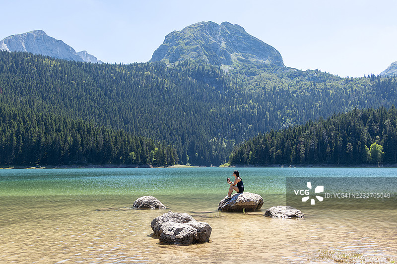 年轻游客在欧洲黑山杜米托尔国家公园的扎布利亚克市镇黑湖畔用智能手机拍照图片素材