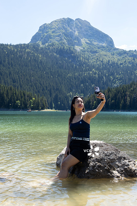 年轻游客在黑湖边用智能手机自拍，该湖位于欧洲黑山杜米托尔国家公园的扎布利亚克市。图片素材