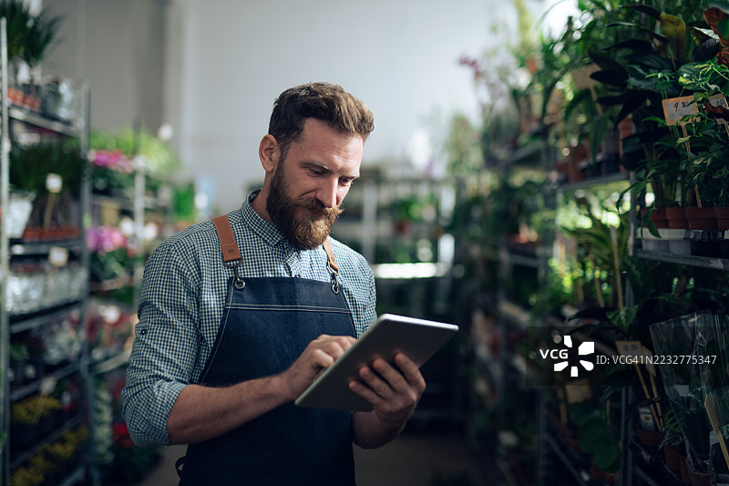 穿着得体的胡子男人在花卉仓库工作。图片素材