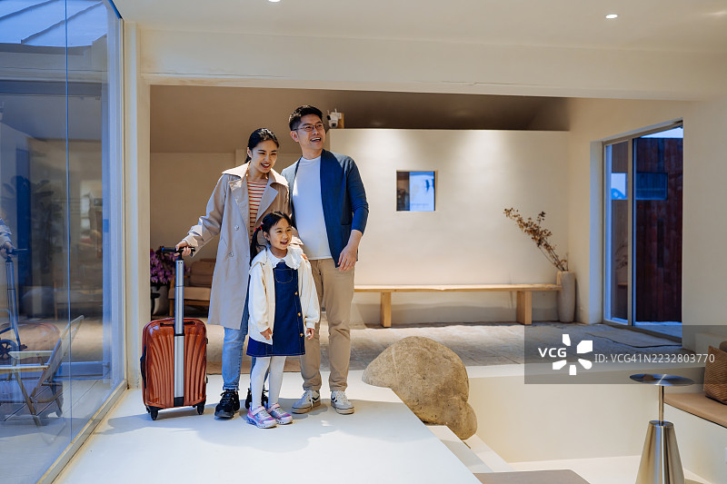 年轻的亚洲家庭在酒店走廊里推着行李。图片素材