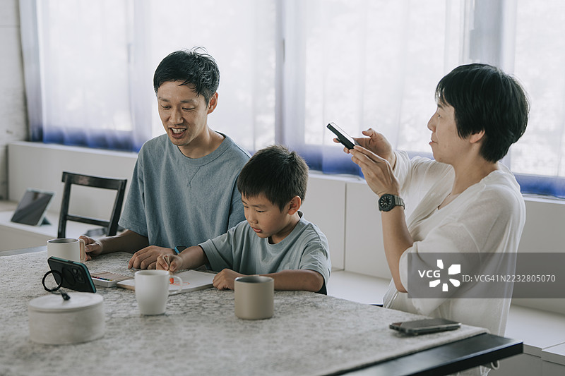 日本家庭在家中共度美好时光，父母和孩子一起使用智能手机和绘画。图片素材