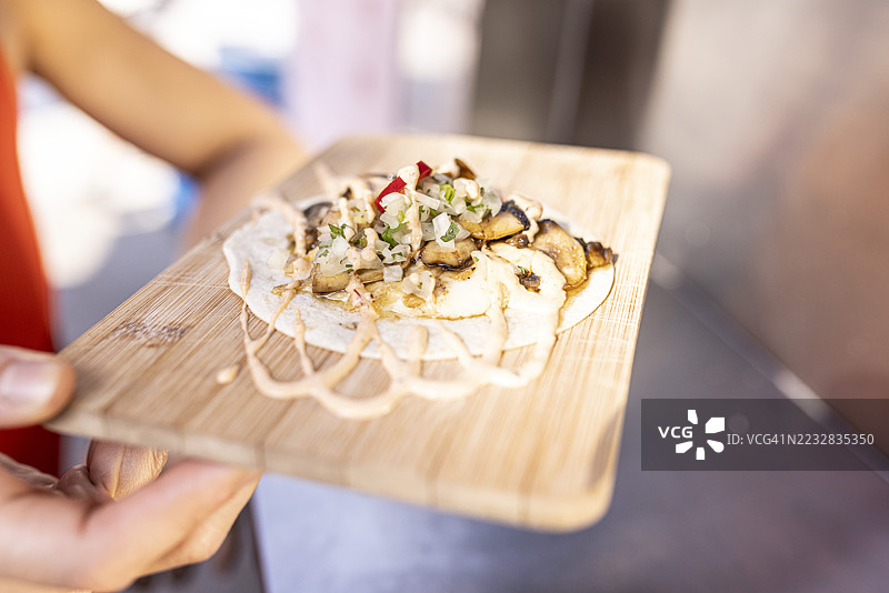 在食品车柜台上，一位女性手持放在木砧板上的现成蔬菜塔可。图片素材