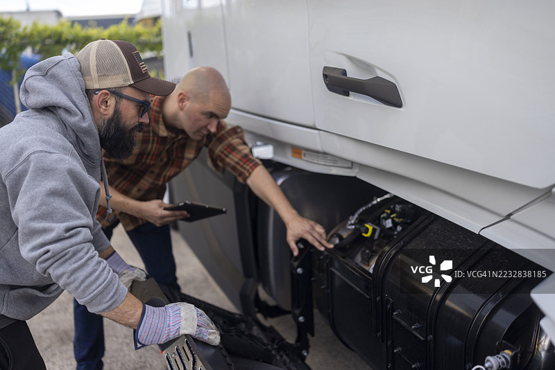 一名卡车司机和一名专业卡车机械师正在讨论卡车的技术问题。图片素材