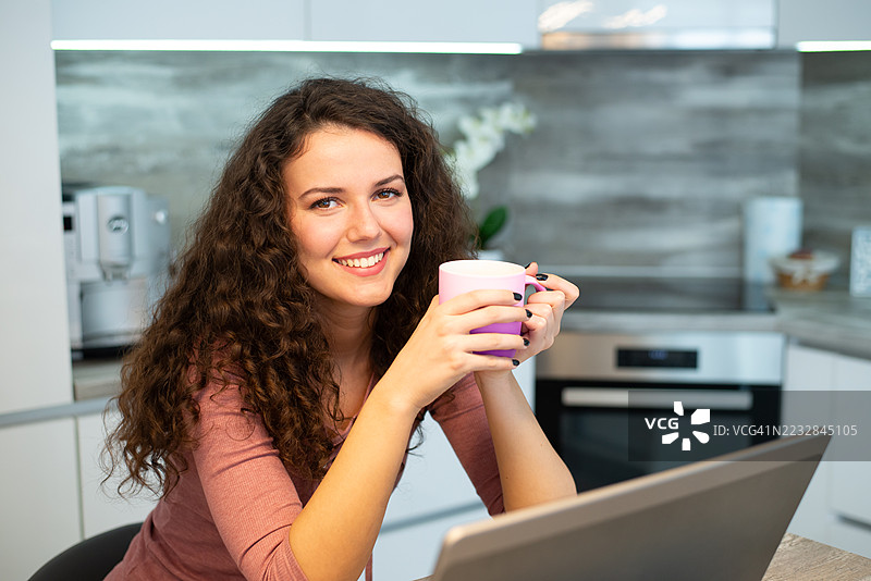 年轻快乐的女性在家喝咖啡并使用笔记本电脑图片素材