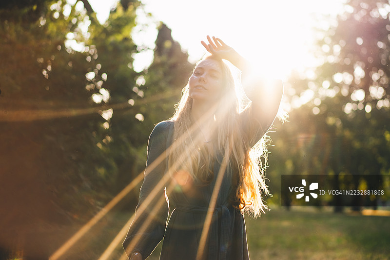 身穿青绿色裙子的波希米亚女性在自然中舞动，金色时光里阳光透过树木洒下。图片素材