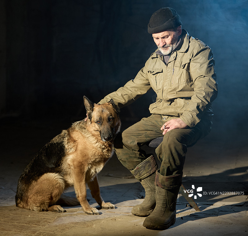 成熟的男人坐在凳子上，沉思地低头，他的狗（德国牧羊犬）坐在主人旁边。图片素材