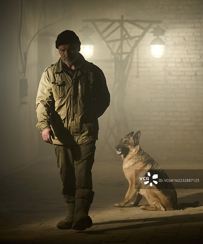 男人正走向砖砌建筑，他的狗（德国牧羊犬）坐在主人身后，悲伤地看着他。图片素材