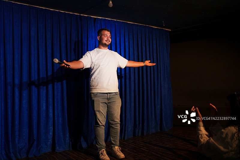 男子在舞台上表演，手持麦克风，双臂张开。图片素材