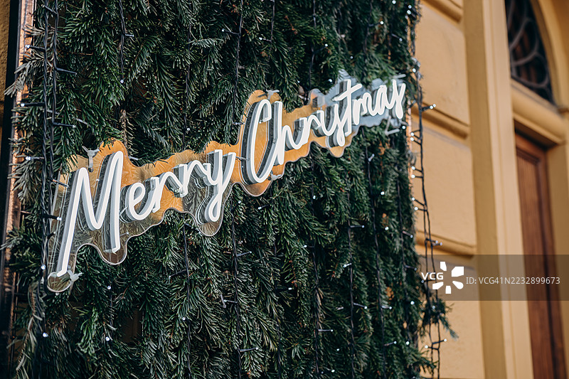 节日装饰，亮起的“圣诞快乐”标志被郁郁葱葱的松枝和闪烁的灯光环绕，营造出欢乐的氛围。图片素材