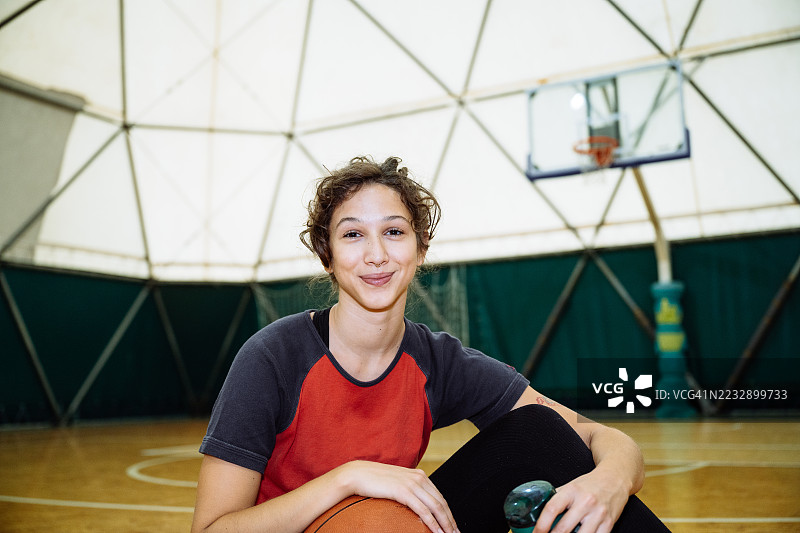 年轻的、意志坚定的女性身穿运动服在室内打篮球，训练后正在休息图片素材