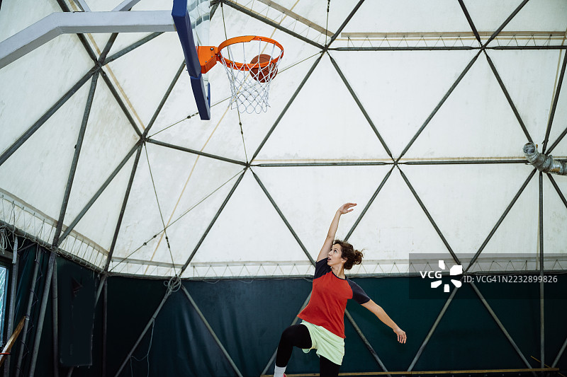 身着运动服的年轻坚定女性在室内打篮球，练习罚球和跳投图片素材