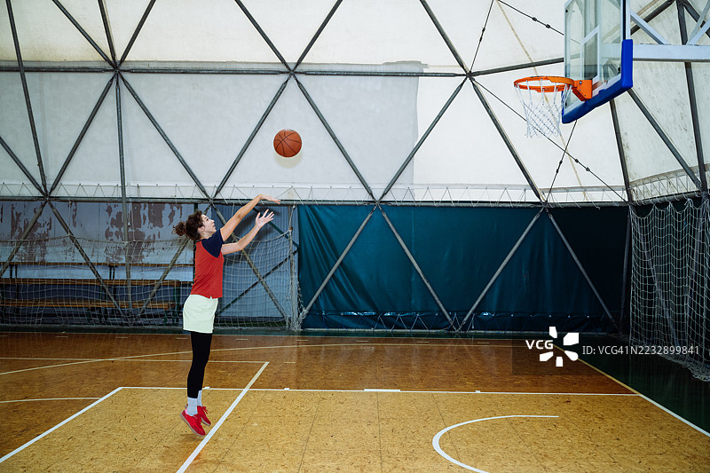 身着运动服的年轻女子在室内打篮球，认真练习罚球和跳投。图片素材
