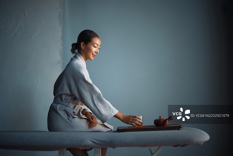 穿着浴袍的女人在简约环境中享受茶饮，放松身心图片素材