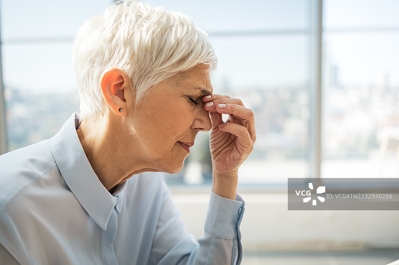 一位老年女性在现代办公室环境中感到不适图片素材
