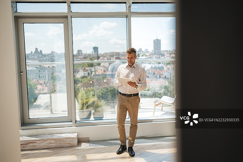 现代办公室中的男子在平板电脑上阅读，背景是城市景观图片素材