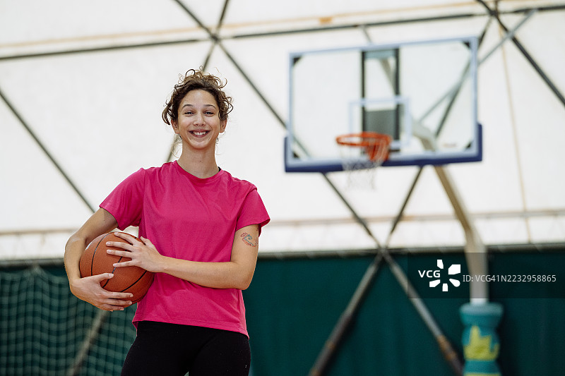 一名自信坚定的女性业余运动员手持篮球，站立并对镜头微笑图片素材