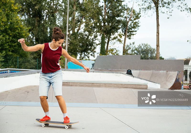 年轻女子在城市建筑背景下的城市滑板公园坡道上练习滑板技巧图片素材