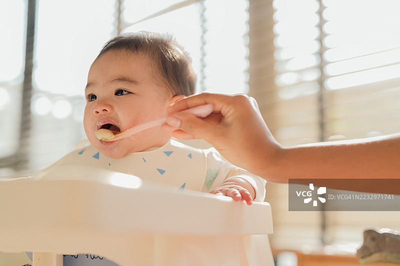 快乐的小女孩微笑着吃着她妈妈喂的自制婴儿泥，捕捉到一个甜美而现代的家庭时刻。图片素材