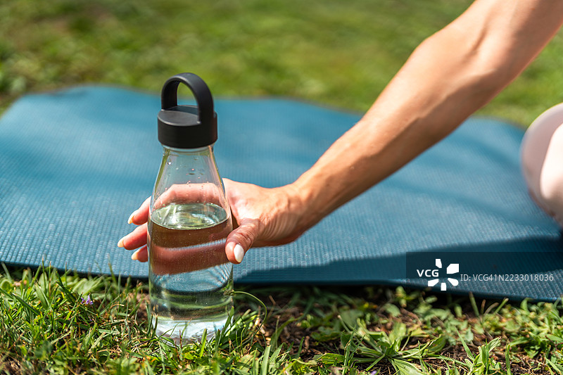 手伸向瑜伽垫上的可重复使用水瓶图片素材
