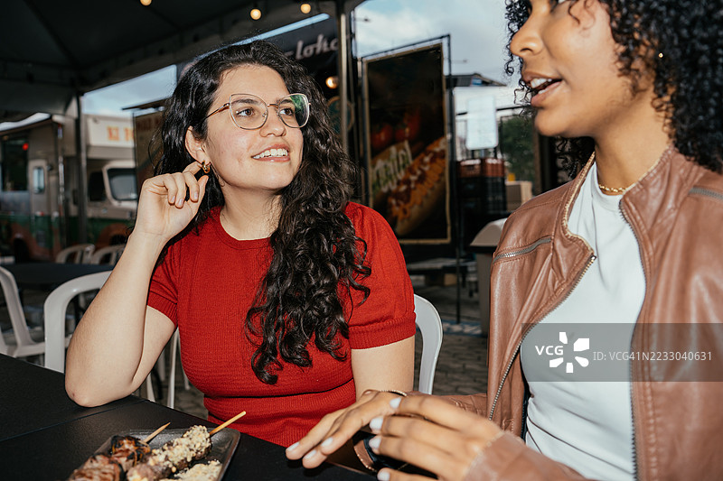 两位女性朋友在餐车享用快乐时光，吃着烤串图片素材