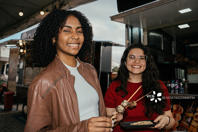 两位女性朋友在餐车享用快乐时光，吃着烤串图片素材
