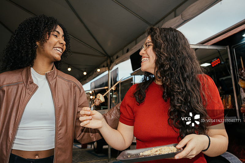 两位女性朋友在餐车享用烤串，享受欢乐时光图片素材