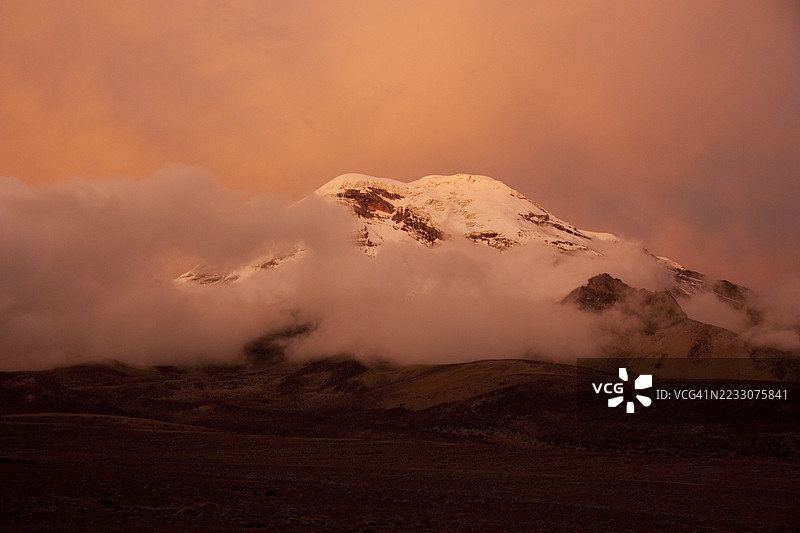 厄瓜多尔的钦博拉索火山在多彩的日落中透过云层若隐若现图片素材