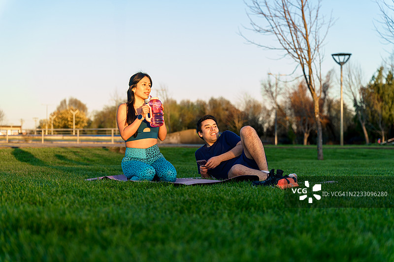 年轻的西班牙裔情侣在训练后休息，喝水并使用手机图片素材