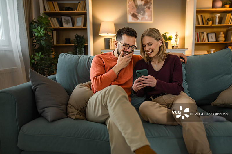 快乐的年轻情侣在家一起使用智能手机。图片素材
