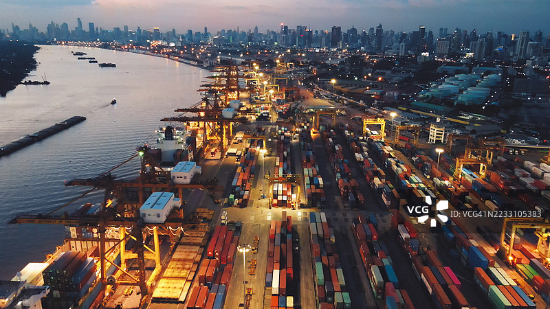 夜间航拍集装箱港口码头物流和全球贸易中心，货运集装箱与城市天际线相映成趣图片素材