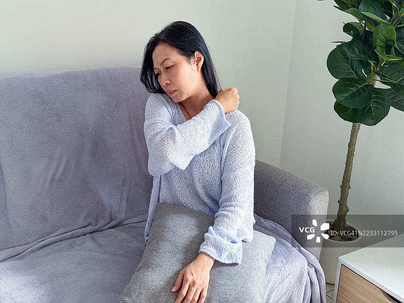 痛苦时刻：年轻女子在家中处理肩部不适图片素材