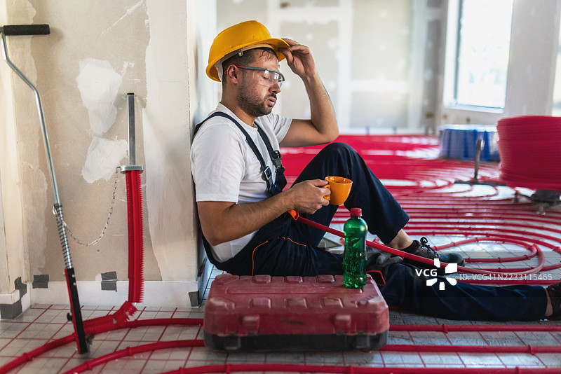 疲惫的建筑工人在安装地暖时休息，喝咖啡。图片素材