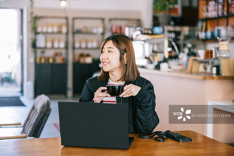 女性在现代咖啡馆享受咖啡，同时使用笔记本电脑工作图片素材