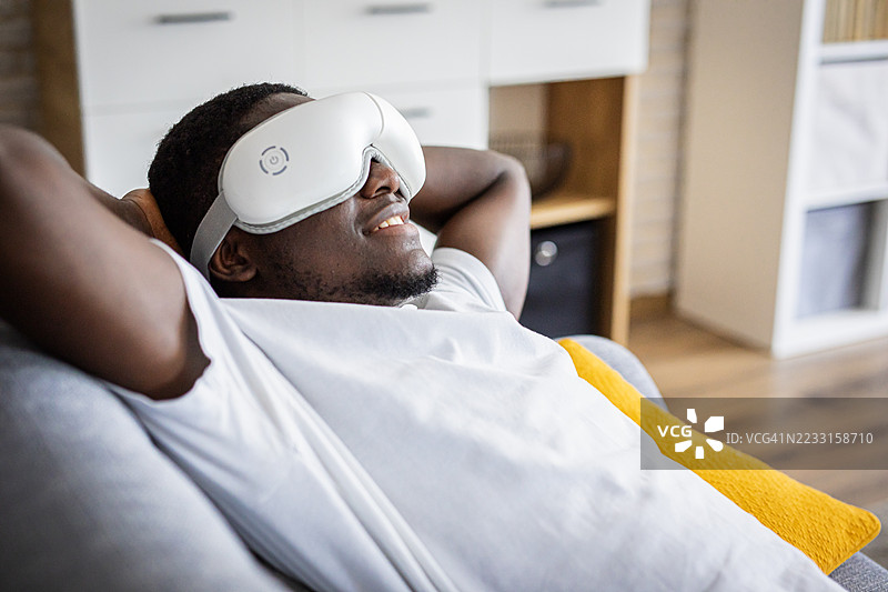 放松的男人躺在沙发上，戴着智能眼罩图片素材