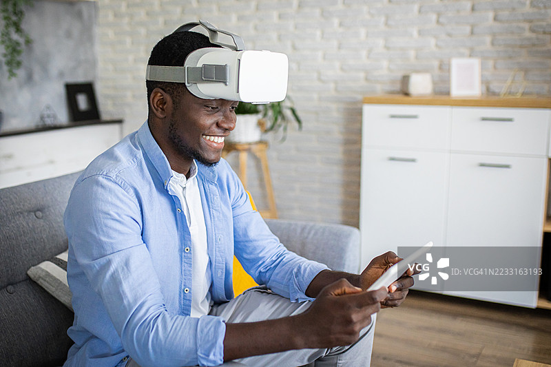 放松的男人在客厅里使用平板电脑和虚拟现实头盔图片素材