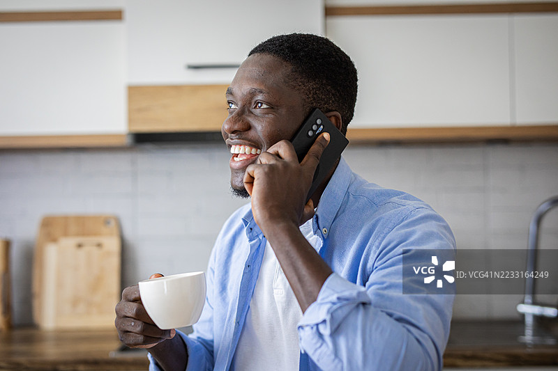 温馨的早晨 – 开心的男人在厨房里喝着咖啡，打电话聊天图片素材