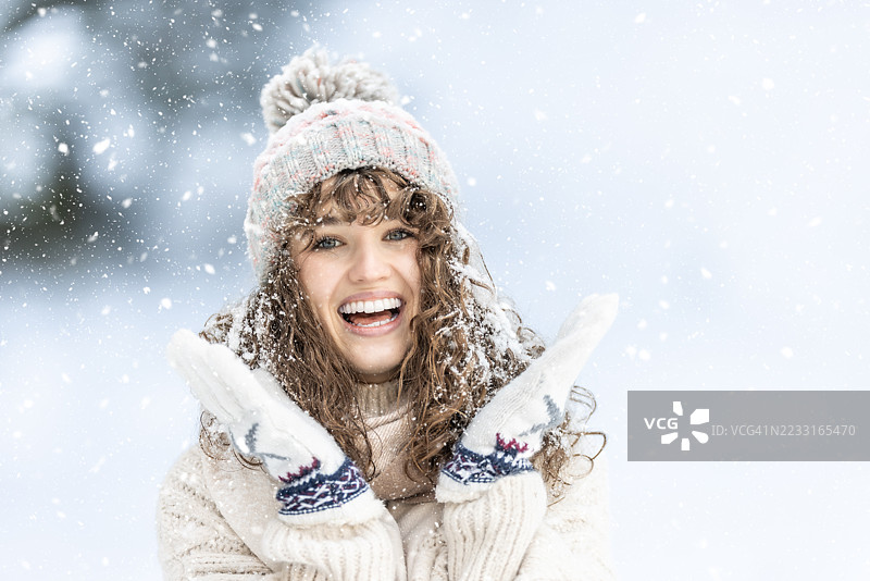 一位美丽的卷发年轻女性穿着针织毛衣、手套和帽子，享受冬天、雪和雪花飘落的时光。图片素材