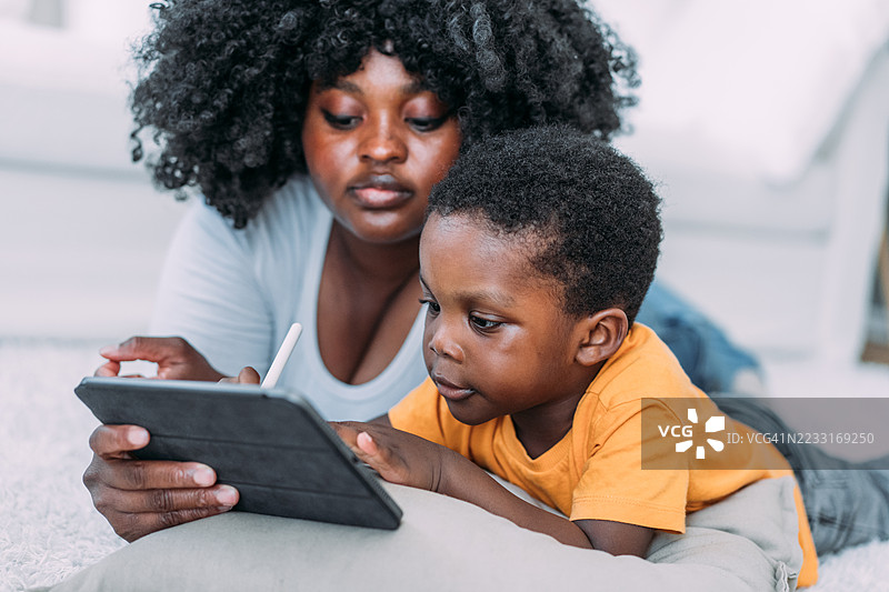 母亲和儿子在家使用平板电脑。图片素材