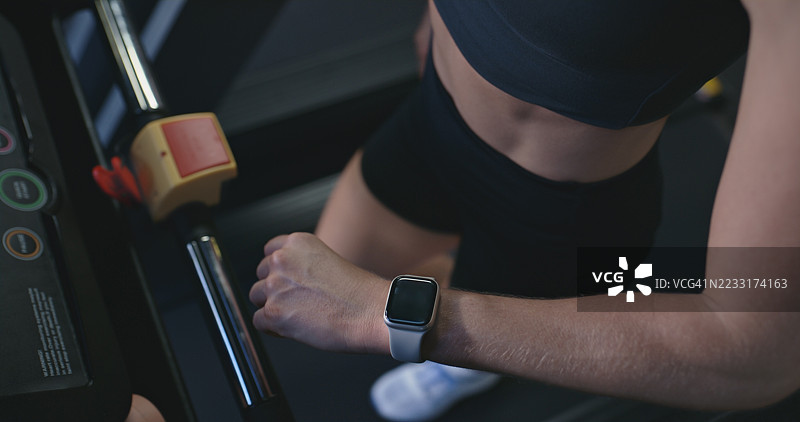 健身房中佩戴智能手表的女性正在使用跑步机，跟踪速度、心率和跑步时间。心肺锻炼、运动应用程序和性能监测，显示个人的进展和统计数据。图片素材